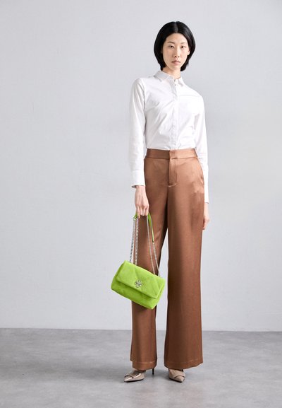 Pantaloni larghi in satin marrone, camicia bianca a maniche lunghe con bottoni, borsa in suede verde con tracolla a catena e tacchi in vernice.