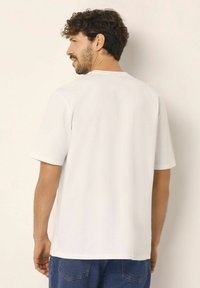 Hvidt kortærmet t-shirt med rund halsudskæring, glat tekstur og afslappet pasform. Bagfra ses rene linjer og et enkelt design.