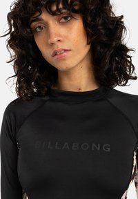 Čierny dlhý rukáv rash guard s matným logom "BILLABONG" na hrudi, s hladkou textúrou a dizajnom raglánových rukávov.