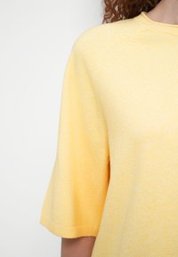 Κίτρινο πλεκτό τοπ με άνετη εφαρμογή, ριμπ λαιμόκοψη και κοντά μανίκια με διακριτικό υφασμένο μοτίβο.