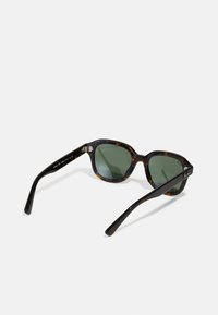 Occhiali da sole tartaruga con lenti verdi, forma rotonda e oversize, e bracci neri eleganti. Dettagli hardware in argento evidenti sulle tempie.