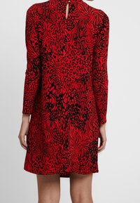 Robe rouge à manches longues, avec un motif animalier noir et un détail en forme de trou à l'arrière. Fabriquée en tissu lisse et extensible.