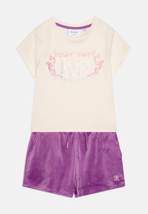Cremefarbenes Kurzarmoberteil mit pinkem Strassstein-„Juicy Couture“-Logo, kombiniert mit lila Velours-Shorts mit Kordelzug.