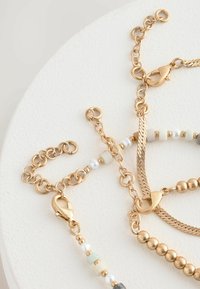 Collane in oro con catene a maglia testurizzata, dotate di piccole perle bianche, verdi e grigie. Inclusi vari tipi di chiusure.