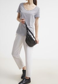 Camiseta de manga corta a rayas en blanco y azul marino, combinada con pantalones blancos y un pequeño bolso negro de hombro. Unos zapatos negros con cordones completan el atuendo.