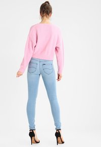 Suéter fuzzy rosa claro de manga larga, combinado con jeans skinny azul claro. El modelo lleva sandalias de tacón alto negras.