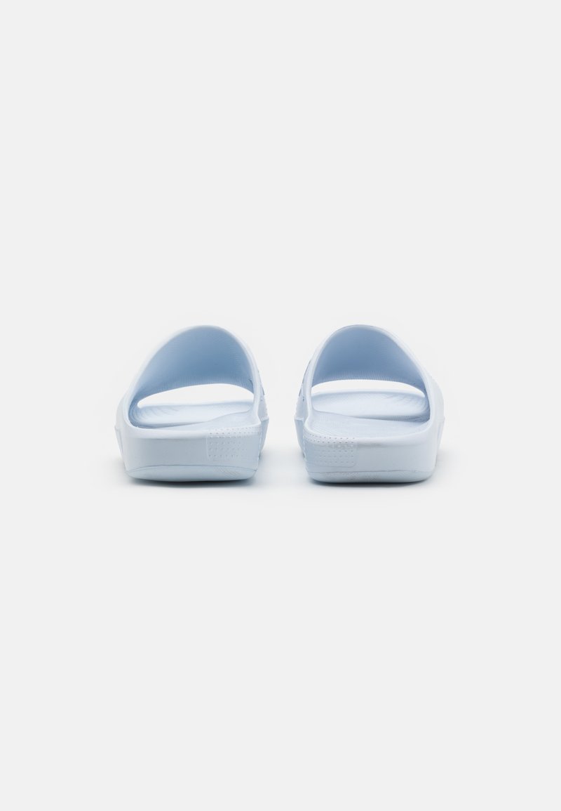 Sandales blanches à glisser avec une texture lisse, arrière ouvert et une légère courbe à la base. Présente un design minimaliste sans motifs visibles.