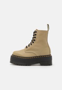 Stivale da combattimento in pelle beige con suola platform nera, lacci neri, cuciture gialle e un'etichetta di marca sul retro.