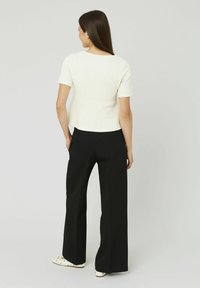Un haut blanc texturé à manches courtes associé à un pantalon noir à jambes larges et des chaussures à enfiler avec des accents décoratifs. Silhouette simple et moderne.