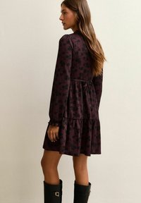 Abito a maniche lunghe color bordeaux con motivo floreale, gonna ampia e vita regolabile con cordino. Indossato con stivali neri al ginocchio.