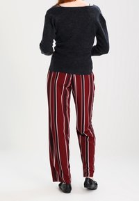 Pull noir à texture avec des manches longues, associé à un pantalon rayé bordeaux. Le pantalon présente des rayures blanches verticales, une coupe à jambes larges et des chaussures plates noires.