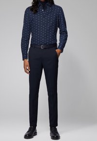 Navy overhemd met knopen en witte stippen, van katoen, gecombineerd met een op maat gemaakt donker broek en zwarte schoenen, wat een formele uitstraling creëert.