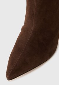 Barna velúr stiletto csizma hegyes orral, sima textúrával és testhezálló szilhouettel, amely kiváló varrással emeli ki a varrásokat.