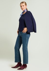 Cárdigan abotonado azul marino, top azul marino, vaqueros azules y tacones puntiagudos burdeos con acabado brillante. Un pañuelo multicolor anudado al cuello.