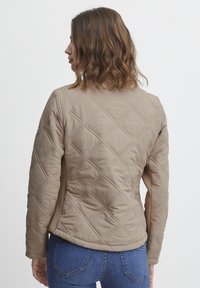 Jachetă bej matlasată cu model în diamante, textură moale și un design ajustat. Prezintă panouri laterale și o siluetă casual.