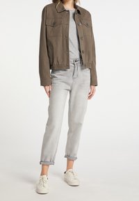 Veste en coton marron avec un devant à boutons, deux poches poitrine et une taille élastique. Associée à un jean gris et des baskets blanches.