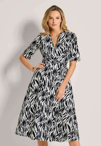 Schwarz-weißer gemusterter Wickelkleid mit V-Ausschnitt, kurzen Ärmeln und definiertem Taillenbereich, das eine fließende A-Linie-Silhouette aufweist.