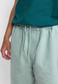Lichtgroene katoenen joggers met een elastische tailleband en een trekkoorddetail. De stof heeft een subtiele textuur en zijzakken.