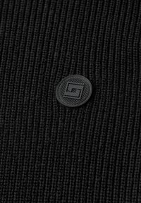 Tissu en tricot noire côtelé avec un patch logo noir rond présentant un design géométrique et une surface texturée.