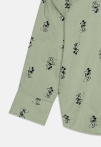 Camicia verde chiaro con una stampa nera ripetuta di personaggi dei cartoni animati. Il tessuto è liscio, con un colletto e dei polsini dal design strutturato.