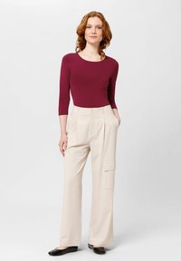 Haut ajusté bordeaux à manches trois-quarts associé à un pantalon large beige taille haute avec poches latérales. Chaussures plates noires.