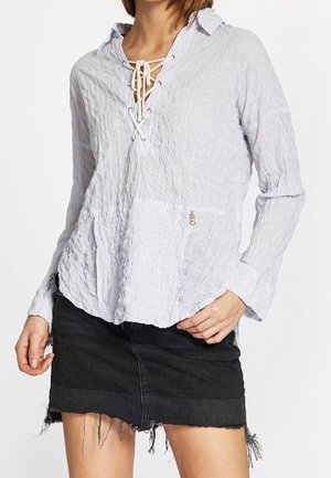 Woman wearing a light gray textured long-sleeve blouse with lace-up neckline and a black frayed denim mini skirt.