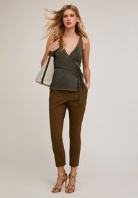Top gris con un lazo en la cintura, combinado con pantalones marrones ajustados. Modelo sosteniendo un bolso de hombro bicolor, usando tacones con tiras.