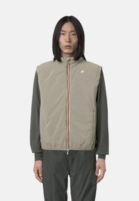 Gilet imbottito beige con colletto alto, zip frontale con strisce multicolori, texture trapuntata e dettaglio logo sul petto.