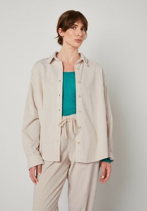 Lichtbeige corduroy overhemdjacket met een kraag en knoopsluiting, gelaagd over een teal top en gecombineerd met bijpassende beige broeken.