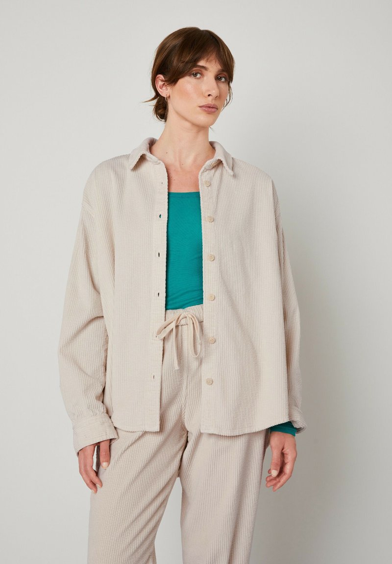 Ljusbeige kordjacka med krage och knapplås, lager på en teal-top och matchande beige byxor.