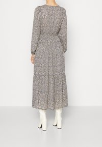 Robe florale à manches longues avec un motif blanc, bleu et beige. Taille élastique, jupe à volants, portée avec des bottes à talons blanches.