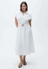 Abito camicia bianco con maniche corte, chiusura a bottoni sul davanti, cintura in vita con fibbia in legno e texture in pizzo. Design fino al ginocchio.