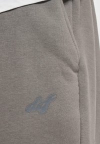 Grå bomull joggebukser med en glatt tekstur, med en blå brodert logo nær lommen. Minimalistisk design med en avslappet passform.