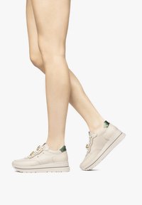Sneaker in pelle beige con suola chunky, dettagli verde sul tallone e parti in oro. Presentano una texture liscia e design con lacci.