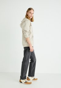 Sweatshirt à capuche beige clair, jeans gris foncé et sneakers beige avec des accents orange. Les vêtements ont une coupe décontractée et des poches latérales.