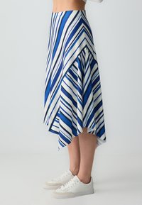 Jupe asymétrique rayée bleue et blanche avec un design évasé, fabriquée à partir d'un tissu côtelé, associée à des baskets blanches.