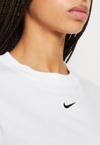 Bílý bavlněný tričko s kulatým výstřihem, na levém horním prsu má malé černé vyšívané logo Nike.