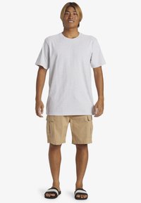 T-shirt en coton gris associé à un short cargo beige doté de poches latérales. Porté avec des sandales à glissière noires et blanches.