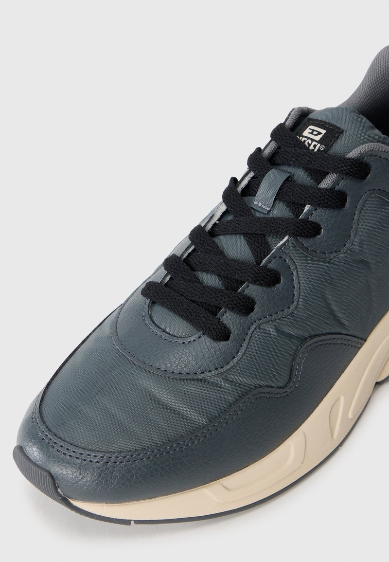 Sneaker da uomo con tomaia in pelle e rete color verde scuro, lacci neri, e una suola intermedia beige con texture, caratterizzata da una punta arrotondata e dettagli imbottiti.