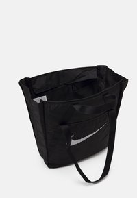 Zwarte Nike draagtas met een wit swoosh-logo, open bovenkant, binnenrits zak en twee lange schouderbanden op een witte achtergrond.