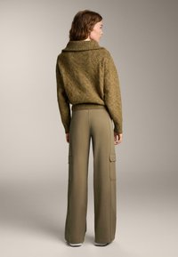Khaki cargo nohavice so bočnými vreckami v kombinácii s textúrovaným olivovo zeleným oversize svetrom s širokým golierom a rebrovaným lemom.