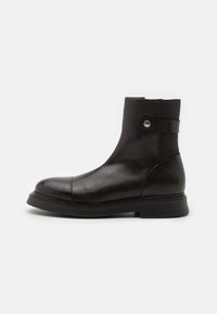 Bottines en cuir noir avec un bout arrondi, un petit talon empilé, un panneau latéral élastique et une sangle décorative avec un détail de bouton en argent.