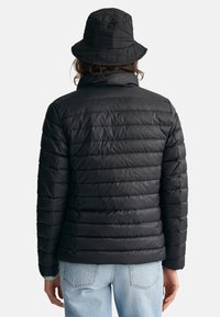 Black puffer jacket with horizontal stitching, high collar, and a relaxed fit. Paired with a matching black bucket hat, textured material.