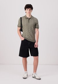 Polo en vert olive avec un motif géométrique, associé à un short noir et des baskets blanches avec des accents noirs. Présente un design à manches courtes.