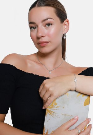 Bijoux en argent comprenant un collier avec pendentif en perle, des boucles d'oreilles assorties et un bracelet. Le mannequin porte un haut noir à côtes décolleté.