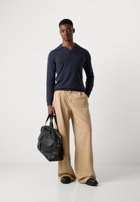 Navy v-neck sweater, cream wide-leg trousers, black leather bag with handles, and black shoes. Simple design, soft materials, and neutral colors.