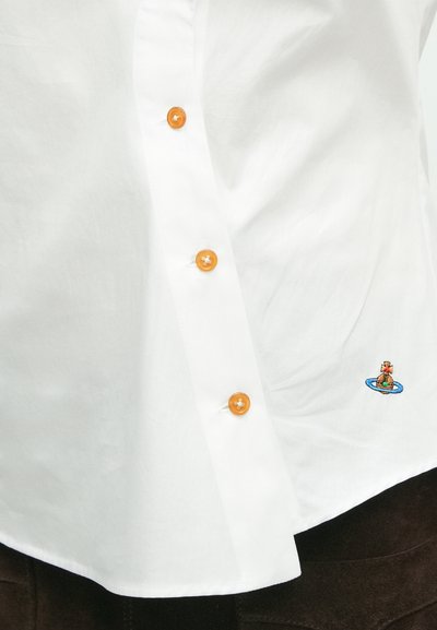 Biela košeľa s piatimi oranžovými gombíkmi a malým vyšívaným vzorom postavy na modrom ovále, umiestnen�á v dolnej ľavej časti. Hladká textúra.