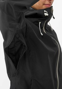 Black waterproof jacket with a high collar, adjustable drawstrings, front zip, and mesh interior pockets. Features minimalistic design.