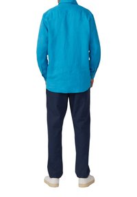 Turquoise linnen blouse met lange mouwen en knoopmanchetten, gecombineerd met een marineblauwe broek. Witte sneakers maken de outfit af.