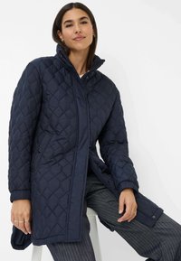 Marineblå quiltet lang frakke med høj krave, knapdetaljer og struktureret diamantmønster. Letvægtsstof med ribbede manchetter.